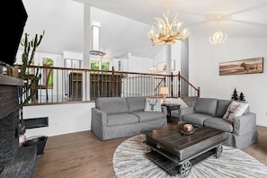 A modern living room with a fireplace, two grey sofas, a coffee table, and a staircase with a railing.