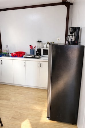 Une cuisine avec des meubles blancs, un réfrigérateur noir, un four à micro-ondes, une machine à café et divers ustensiles de cuisine.
