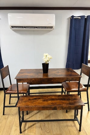 A dining area with a wooden table, four chairs, a bench, a vase with flowers, and an air conditioning unit mounted on the wall. - Casa Lucca, Christmas Bar (Barra de Navidad)