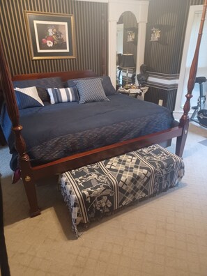 Ein Bett mit Baldachin, ausgestattet mit einem dunkelblauen Überwurf und passenden Kissen, einer gemusterten Tagesdecke sowie einem passenden Fußteil.