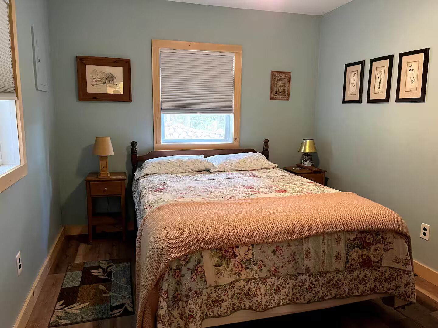 A bedroom with a bed, a window with blinds, a bedside table with a lamp, and a rug.