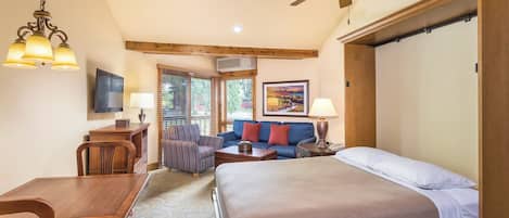 A hotel room with a bed, a dining table, a sofa, a TV, and a ceiling fan.