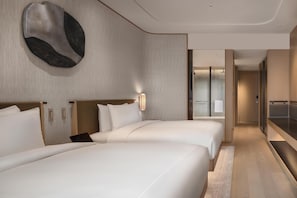 Habitación de hotel con dos camas, un espejo grande y vista al baño.