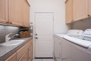 A laundry room with a washing machine, dryer, sink, and cabinets. - The Lookout Palm Springs | Stunning Views (Palm Springs)
