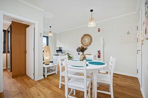 A dining area with a round table, white chairs, a hanging light fixture, and a wall-mounted mirror. - Imperatriz 2D by Homie (Funchal)