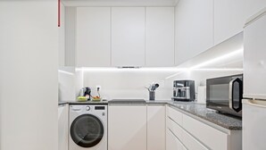 Een kleine keuken met een wasmachine, een koffiezetapparaat en een magnetron.