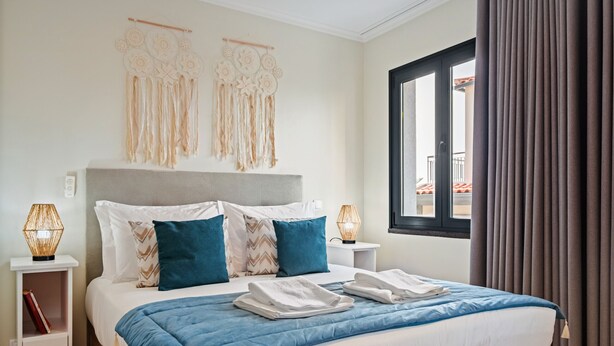 Een hotelkamer met een bed, kussens, een bedlampje, een raam met gordijnen en een decoratie aan de muur.