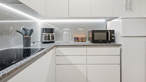 Een moderne keuken met witte kasten, een zwart inductiekookveld, een koffiezetapparaat, een magnetron en een koelkast.
