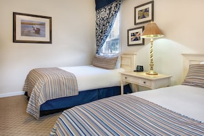 A hotel room with two beds, a nightstand with a lamp, and framed pictures on the wall.