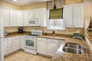 A kitchen with white cabinets, a microwave, a stove, a sink, and a window with curtains.