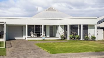 A modern two-story house with a garage, a covered porch with outdoor seating, and a well-maintained lawn.
