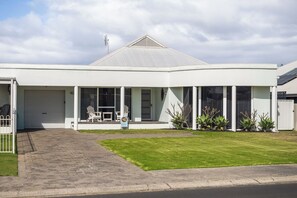A modern two-story house with a garage, a covered porch with outdoor seating, and a well-maintained lawn. - The Bay House - Geographe (Geographe)