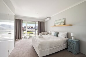Quarto de hotel com uma cama grande, uma escrivaninha com luminária, uma cadeira e vista para a praia através de uma porta deslizante.