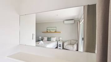 A bedroom with a large mirror, a bed, a chair, a bedside table, and a wall-mounted air conditioner.