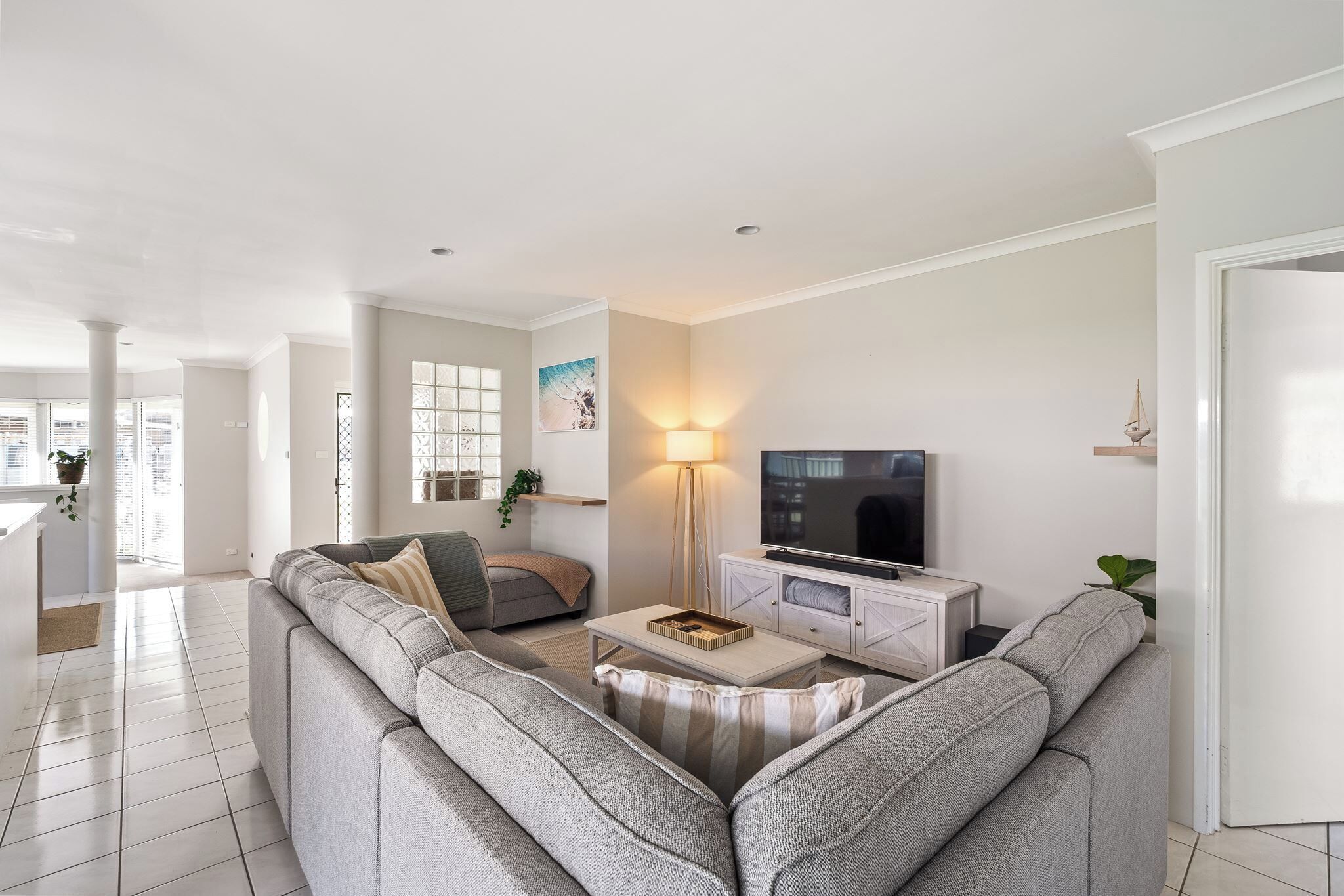 A modern living room with a grey sectional sofa, a coffee table, a TV on a white cabinet, and a floor lamp.