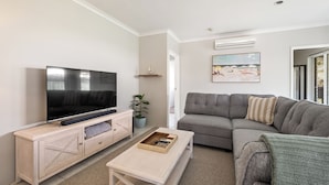 Ein Wohnzimmer mit Flachbildfernseher, grauem Sofa, Couchtisch und einer Topfpflanze.