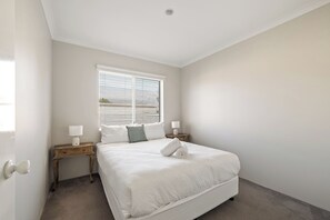 A bedroom with a bed, a nightstand, a lamp, a window with blinds, and a door.