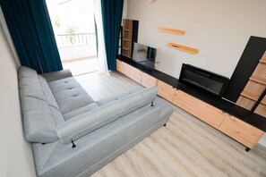 A modern living room with a grey sofa, wooden cabinets, a flat-screen TV, and a balcony with blue curtains. - Once Upon A Haven Setubal (São Lourenço)