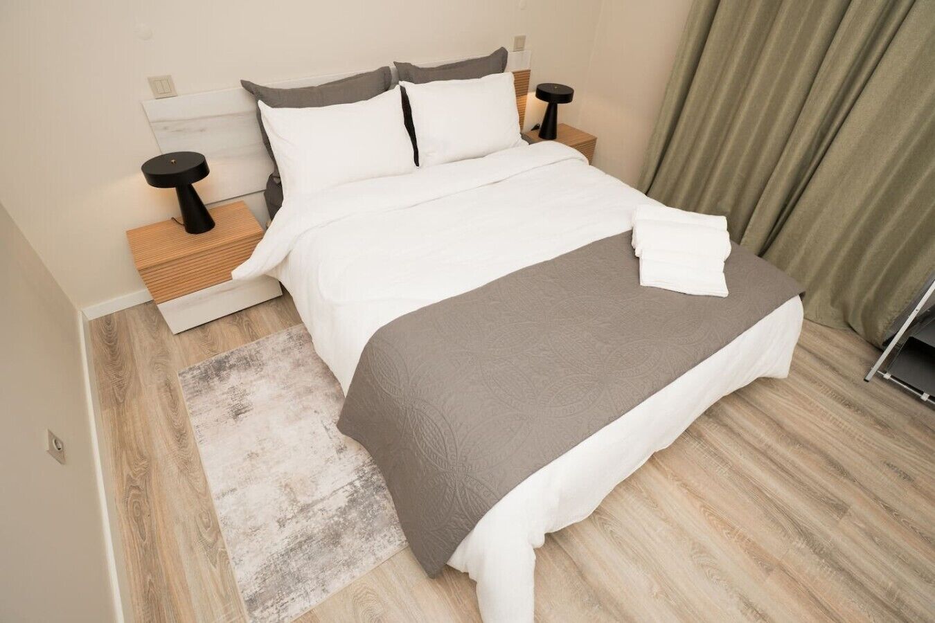 A neatly made bed with a grey throw blanket, two bedside tables with black lamps, and a wooden headboard.