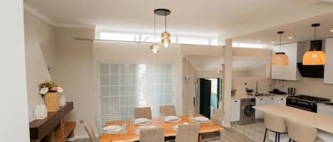 A modern kitchen with a built-in oven, a dining area with a wooden table and chairs, and a kitchen island with bar stools.