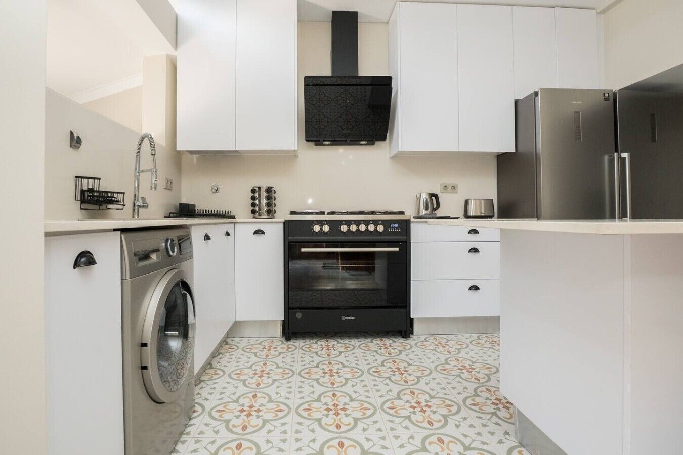 A compact kitchen with a washing machine, oven, and stainless steel refrigerator.