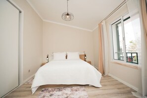 A bedroom with a bed, bedside lamps, a hanging light fixture, a window with curtains, and a view outside. - Once Upon A Haven Setubal (São Lourenço)