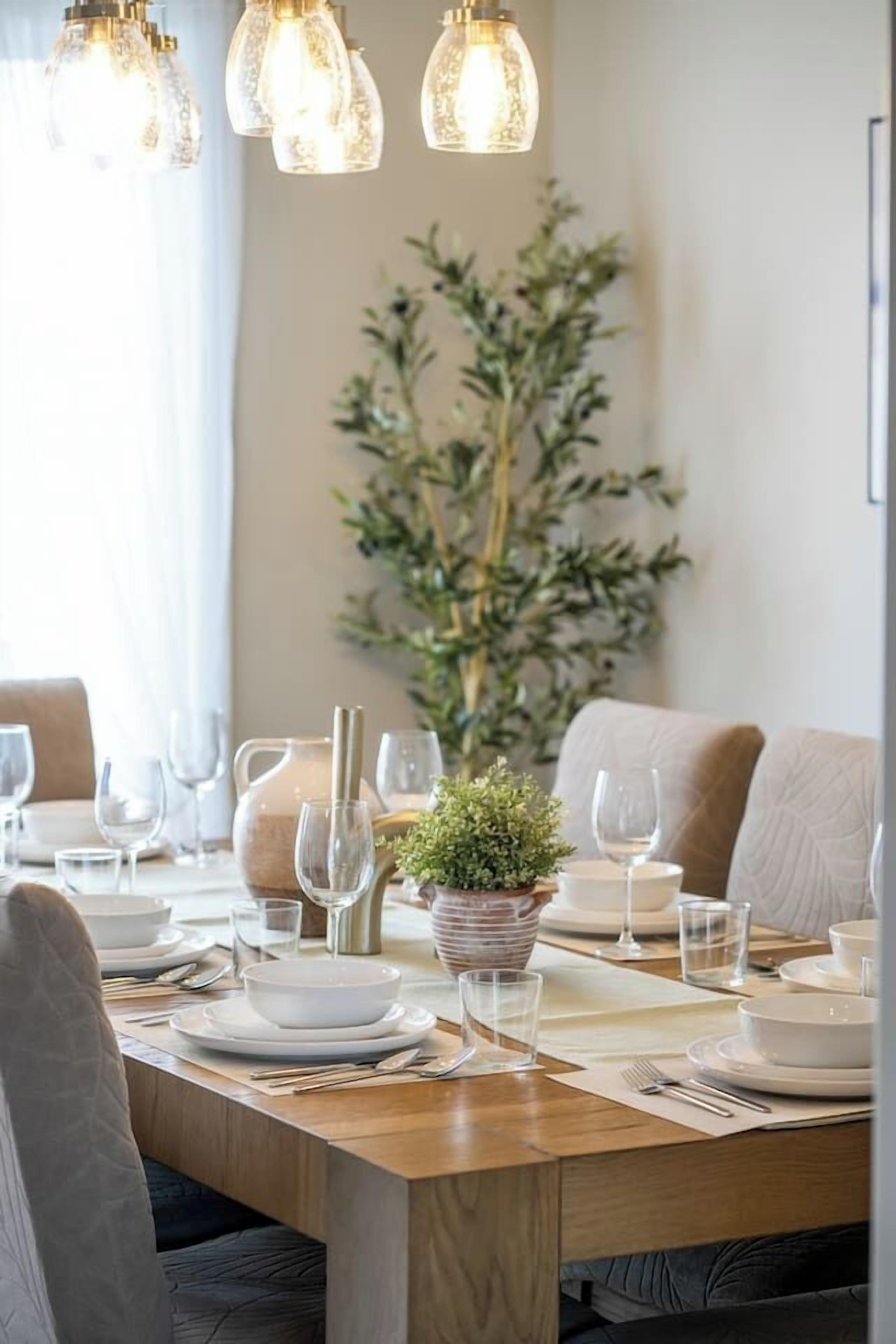 Une table à manger dressée avec des assiettes, des verres et des couverts, agrémentée d’une plante en pot et d’une carafe.