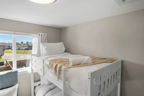 A bunk bed with white bedding, a window with curtains, and a view of a residential area.