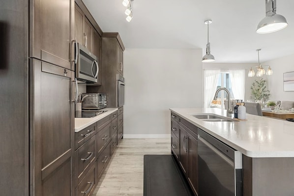 A modern kitchen with dark wood cabinets, stainless steel appliances, and pendant lighting.