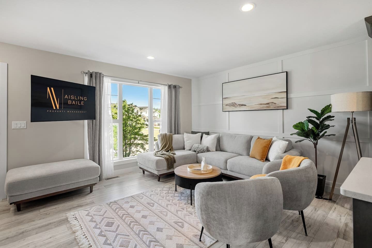 Un salon moderne avec un canapé gris, des fauteuils, une table basse et un téléviseur à écran plat fixé au mur.