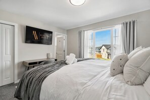 Une chambre avec un grand lit, un bureau, un téléviseur fixé au mur et une vue sur l’extérieur.