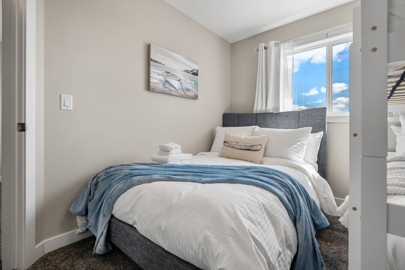 Une chambre à coucher avec un lit, des oreillers, une couverture, un tableau au mur et une fenêtre avec des rideaux.