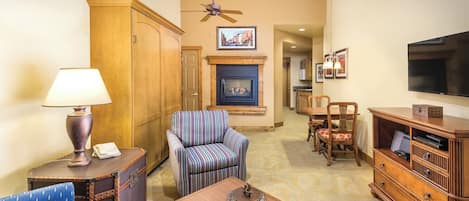 A living room with a fireplace, a television, a dining area, and a hallway.