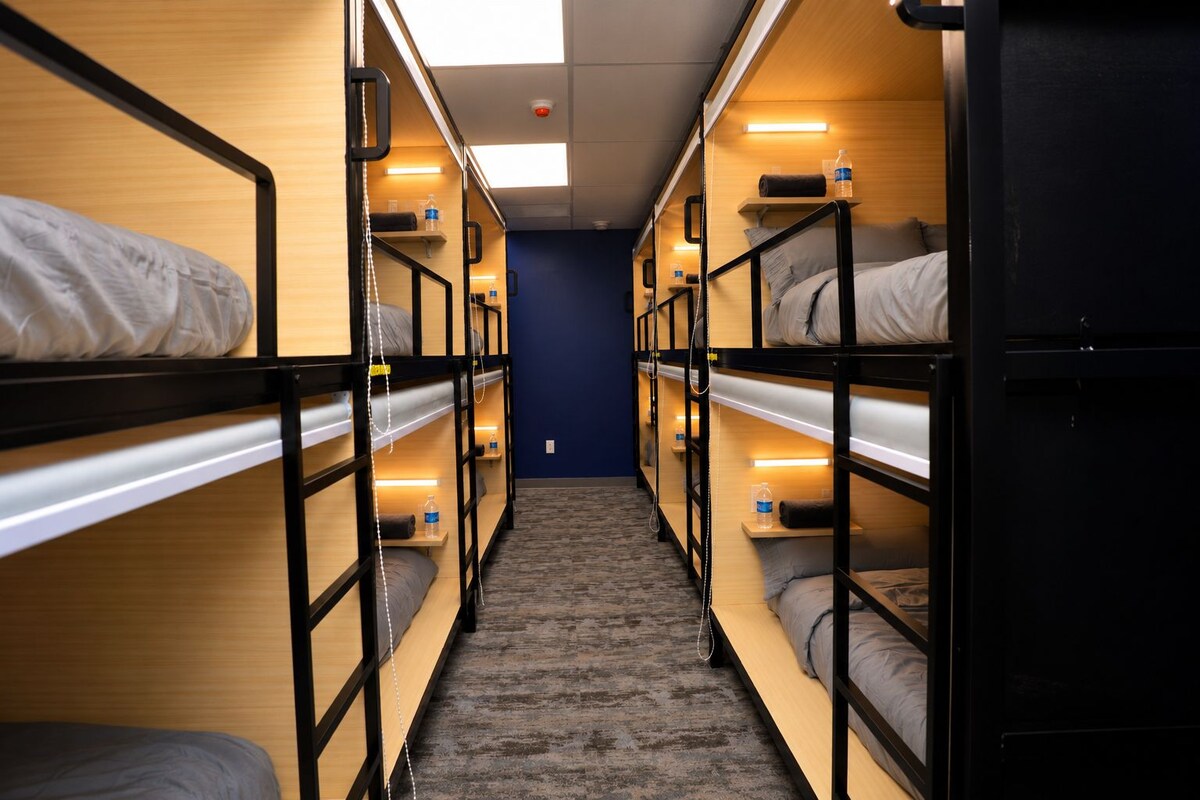 A narrow corridor with bunk beds on either side, wooden walls, and overhead lighting.
