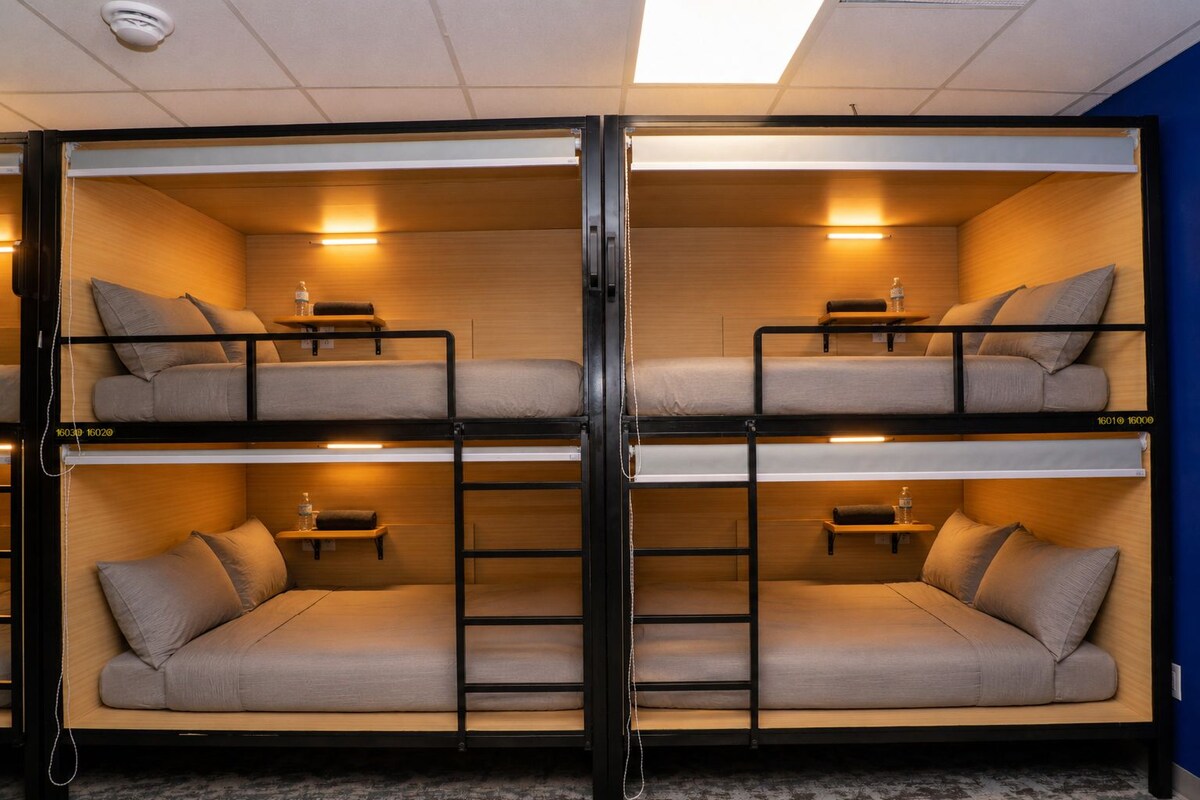 A bunk bed room with two beds, each with a pillow and a small table.