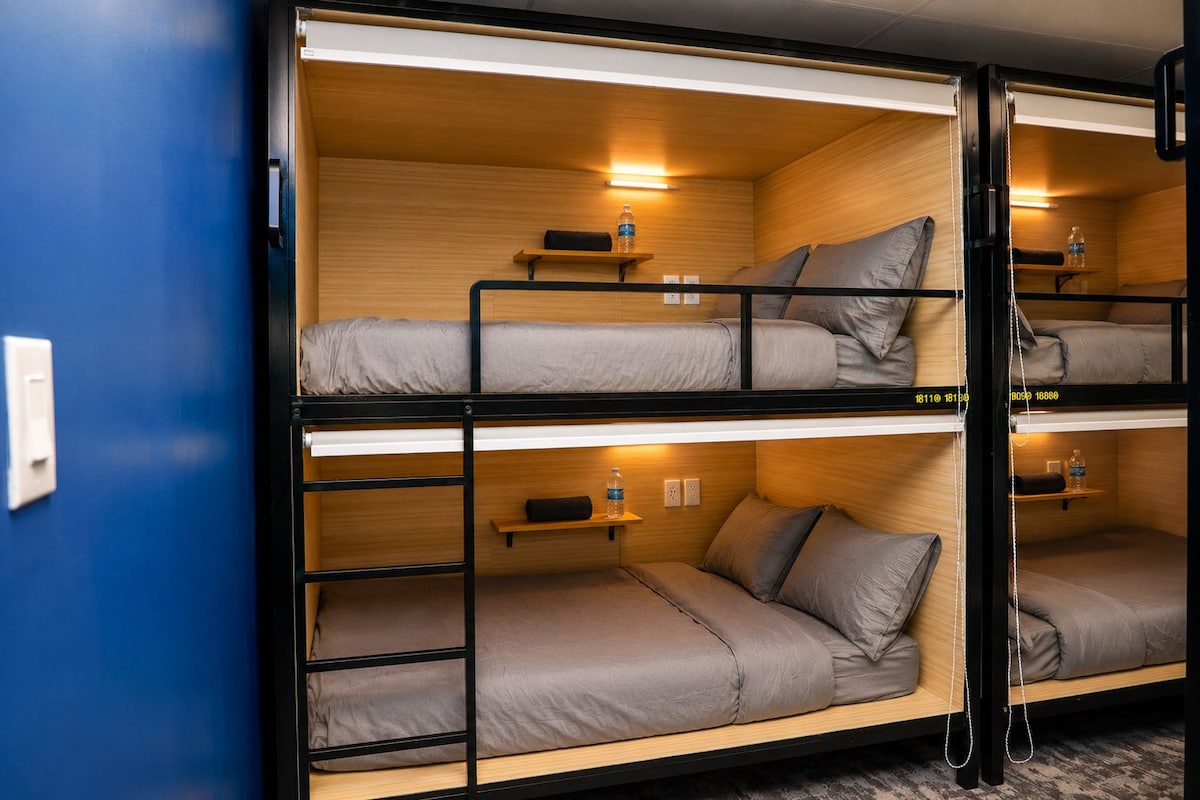 A bunk bed room with wooden walls, a shelf with a water bottle, and a power outlet.