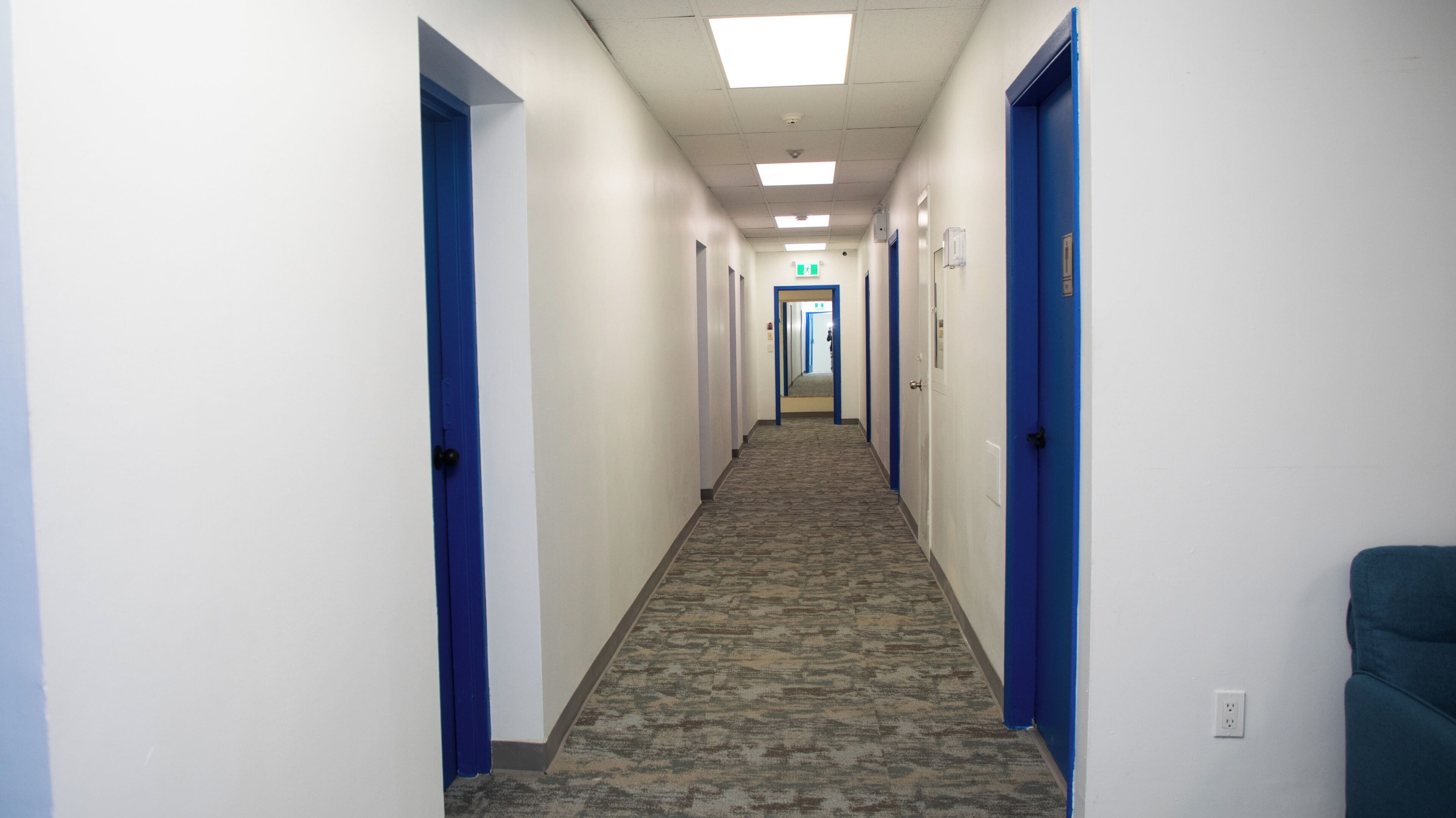 A hotel hallway with carpeted floors, blue doors, and a straight layout.