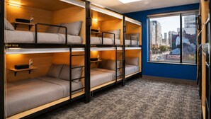 A dormitory room with bunk beds, a window with a city view, and a carpeted floor.