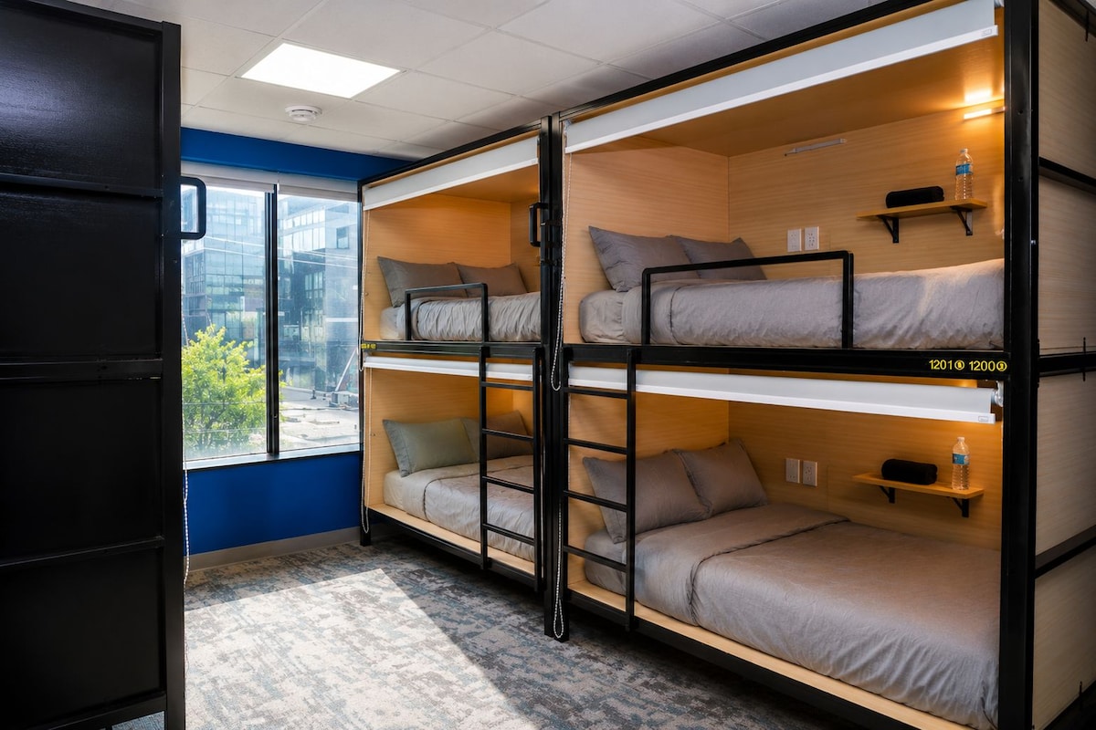 A bunk bed room with a view of a cityscape through a window.