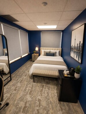 A hotel room with a large bed, bedside tables, a desk with a chair, a mirror, and a cityscape painting on the wall.