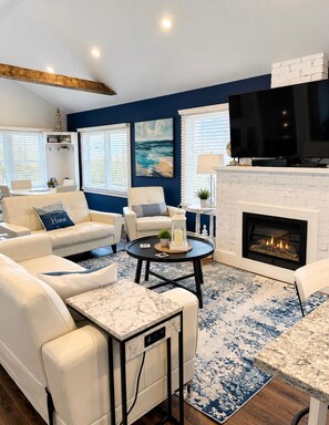 A modern living room with a fireplace, white sofas, a TV, and a blue accent wall. - Crystal Beach Long Term Coastal Cottage (Fort Erie)