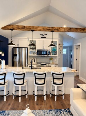 A modern kitchen with white cabinets, stainless steel appliances, and a wooden ceiling beam. - Crystal Beach Long Term Coastal Cottage (Fort Erie)
