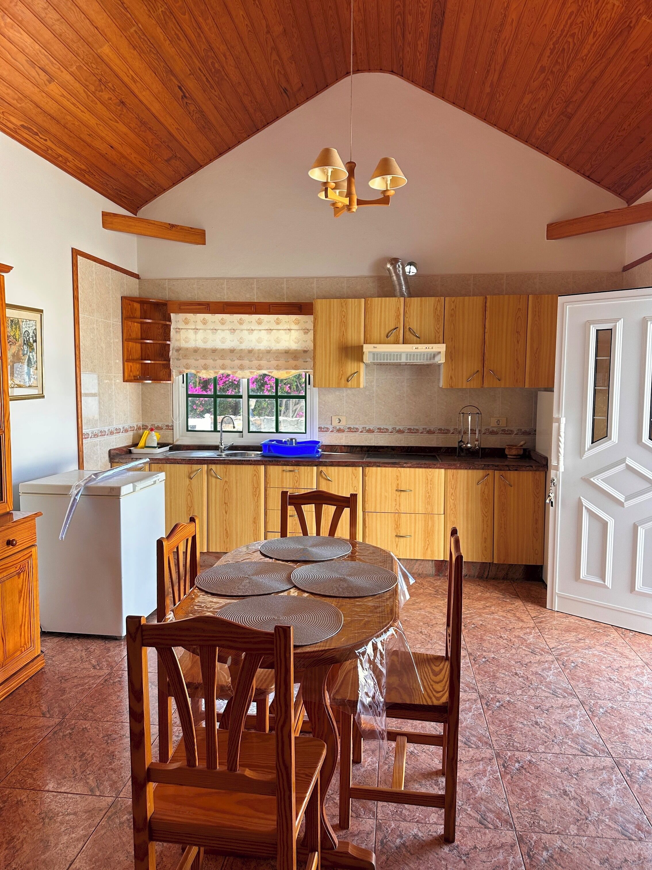 Una cocina con armarios de madera, una mesa de comedor con sillas y un refrigerador.