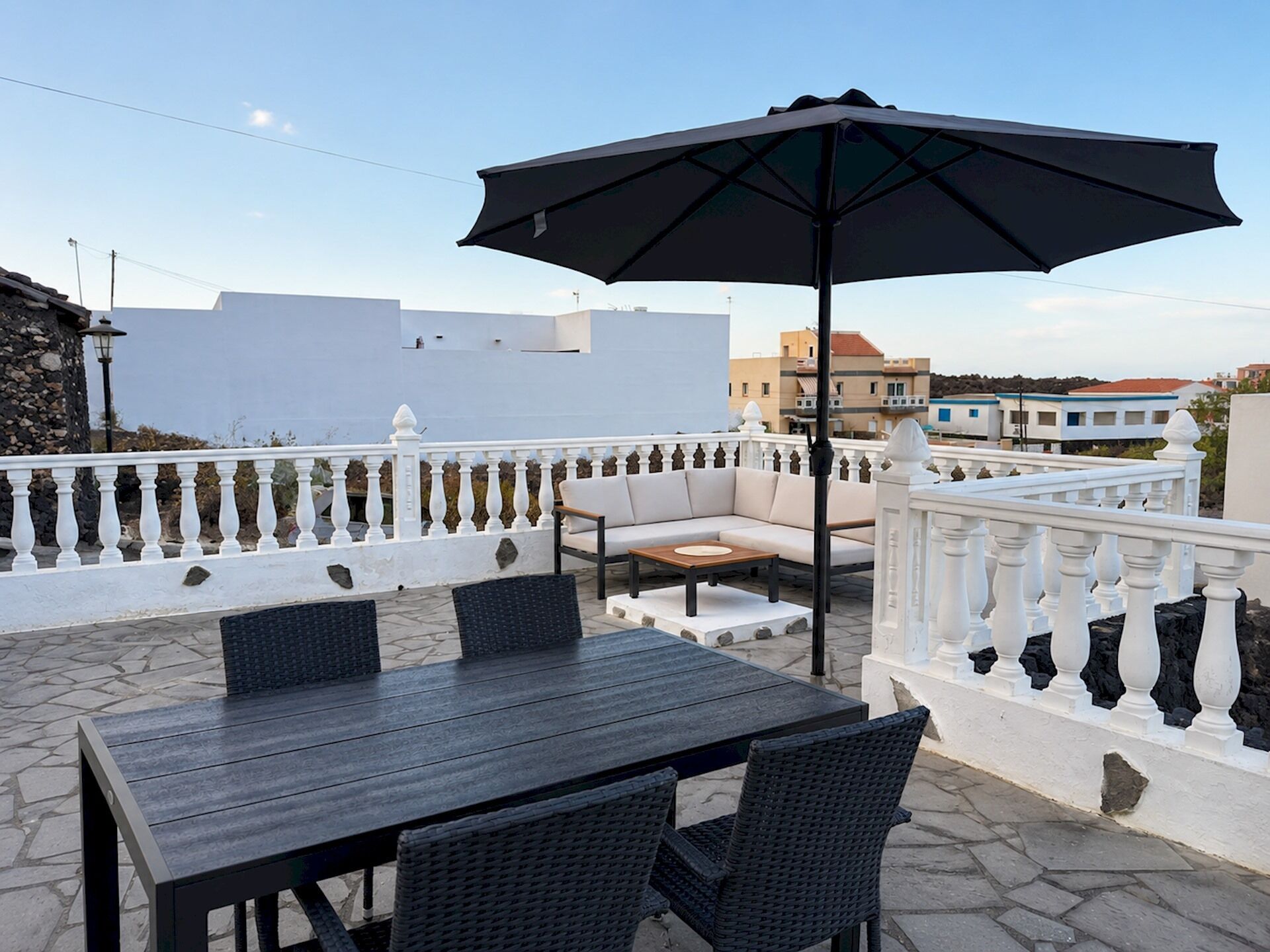 An outdoor patio with a table and chairs, a large umbrella, and a white balustrade.