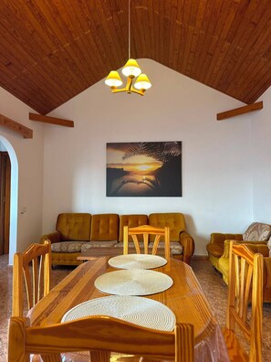 Ein Essbereich mit Holztisch und -stühlen, einer gelben Pendelleuchte und einem Sonnenuntergangsbild an der Wand.