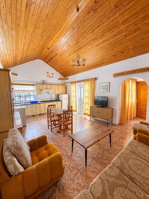 A spacious living area with a high wooden ceiling, a dining table with chairs, and a sofa.