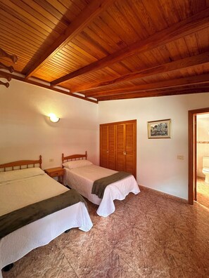 Ein Schlafzimmer mit zwei Einzelbetten, Holzbalkendecke, einer Wandleuchte, einem Holzschrank und einem gerahmten Bild.