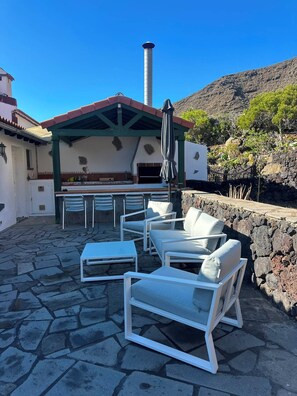 An outdoor patio with stone flooring, white furniture, and a covered seating area with a chimney. - El Rinconcito Home in Tamaduste 5 Min from Beach (Tamaduste)