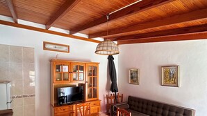 A dining area with a wooden table and chairs, a sofa, a television, and a cabinet with glass doors. - El Rinconcito Home in Tamaduste 5 Min from Beach (Tamaduste)