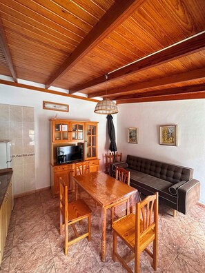 Ein Essbereich mit Holztisch und Stühlen, einer Couch, einem Fernseher und einer Vitrine.